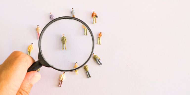 Man with magnifying glass honing in on single figurine represents hiring staff looking to fill Atlassian jobs