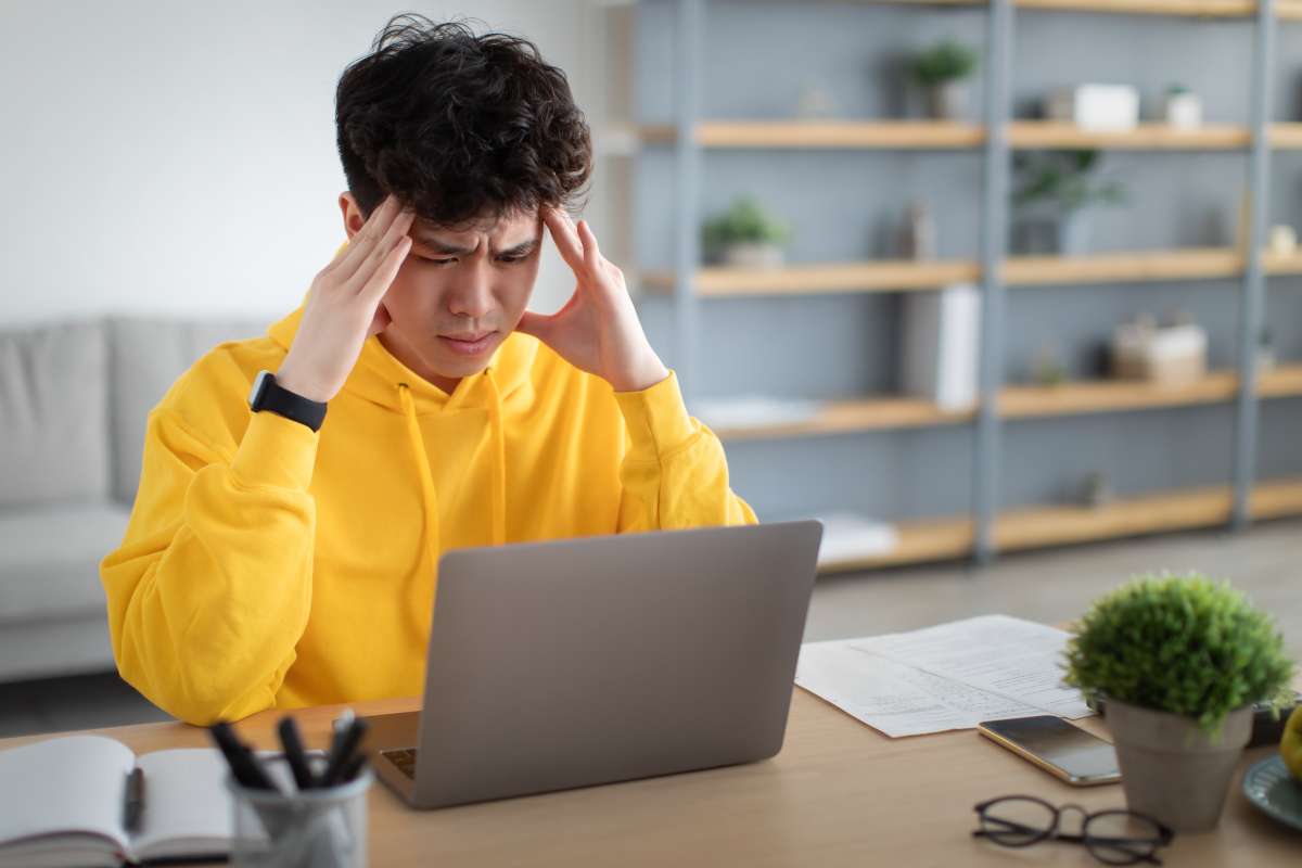 Stressed male asian student in front of a laptop.