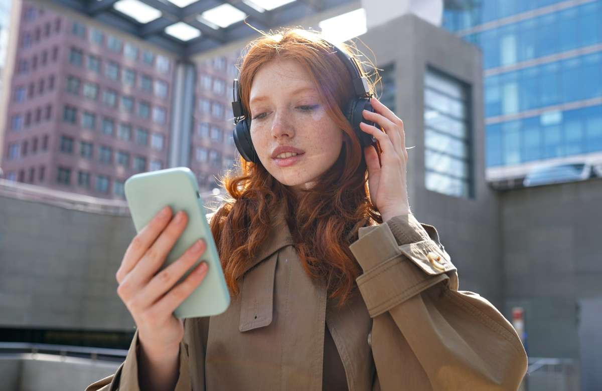 Red headed girl in trenchcoat holding phone, wearing headphones