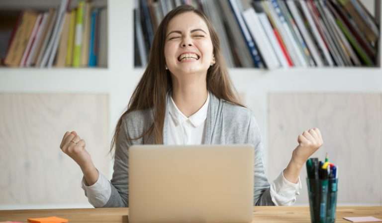 Woman with long brown hair looking excited in front of a laptop