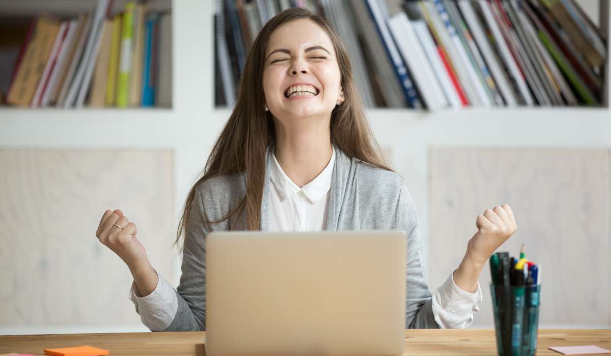 Woman with long brown hair looking excited in front of a laptop