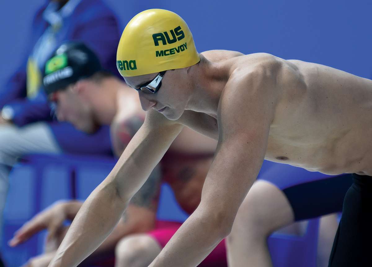 Person about to dive into water wearing yellow swim cap that says McEvoy.