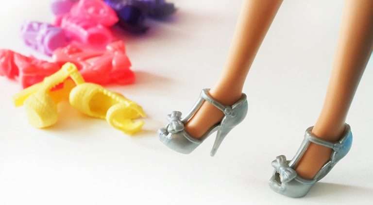 Legs of a Barbie doll, wearing high heeled shoes, and some other shoes in different colors are on the back side.
