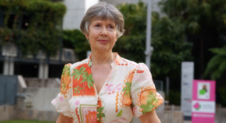 Woman with short grey hair, wearing a brightly patterned dress.
