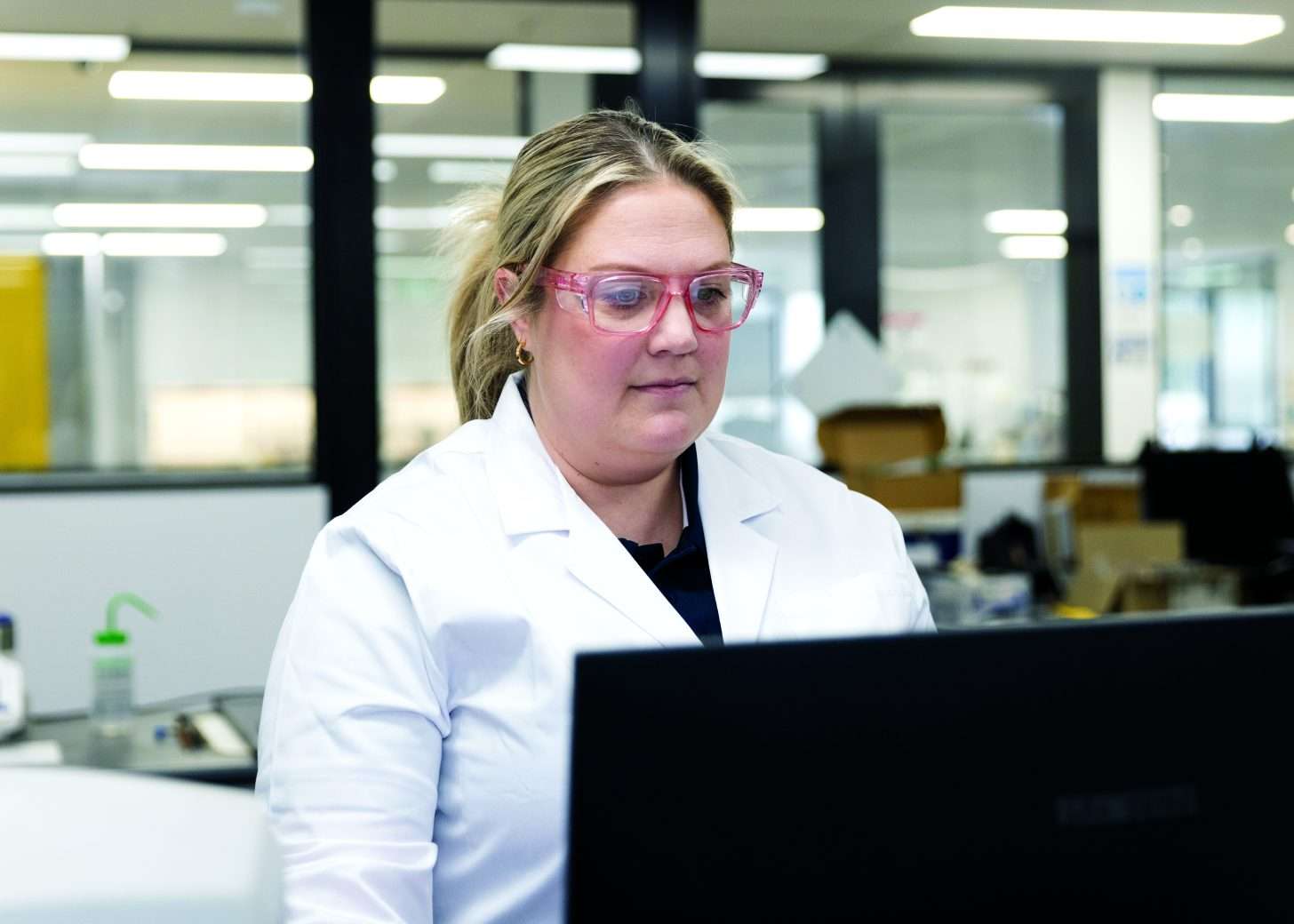 Woman in white labcoat behind computer