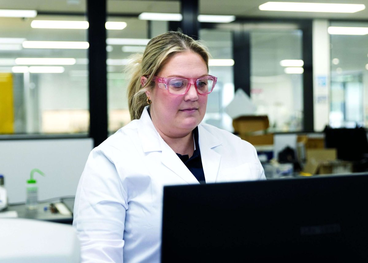 Woman in white labcoat behind computer