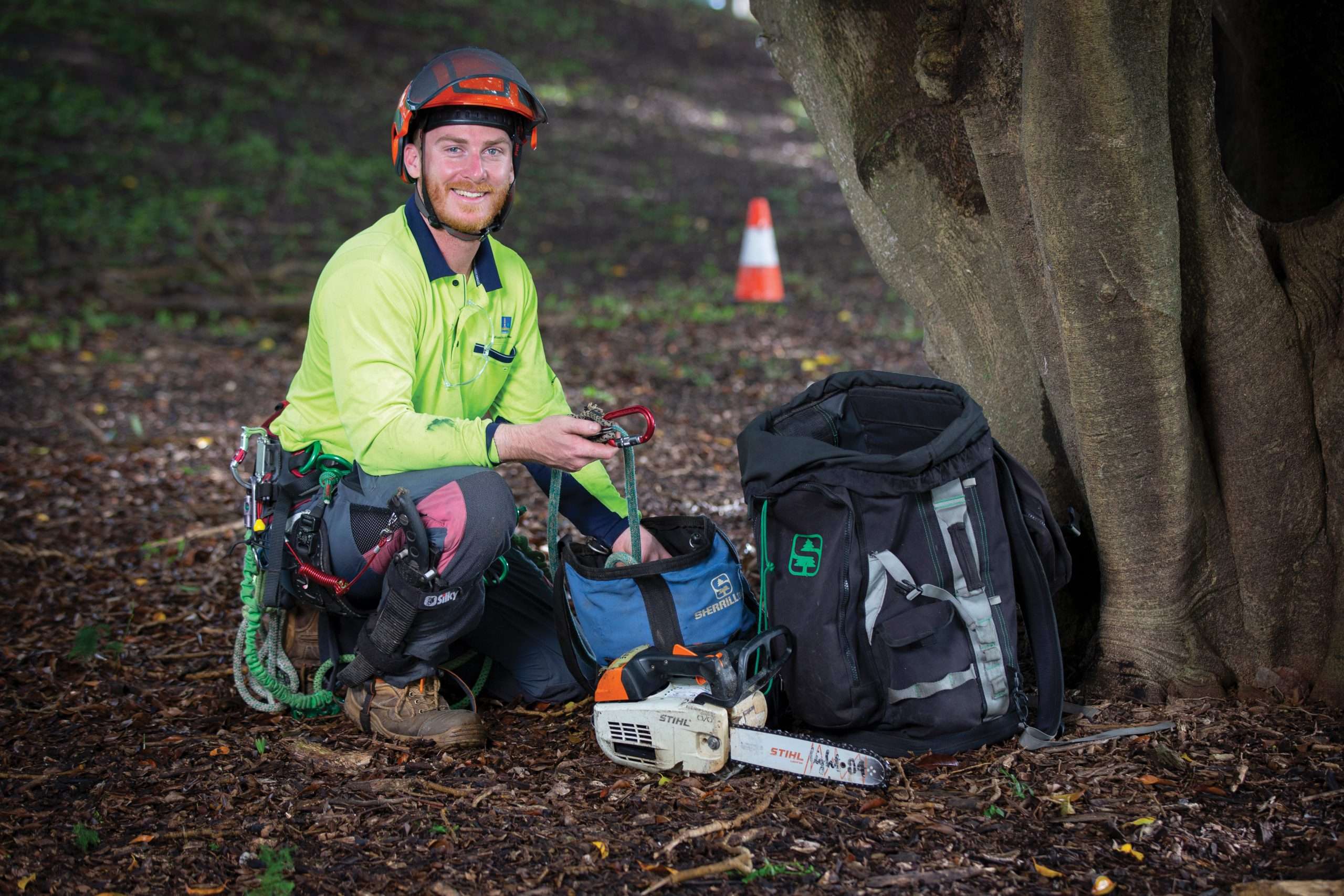 Person wearing high vis and orange helmet in front of a tree