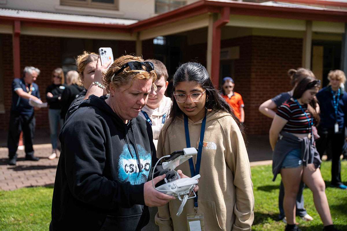 Person in CSIRO jumper holding remote control, standing next to a student