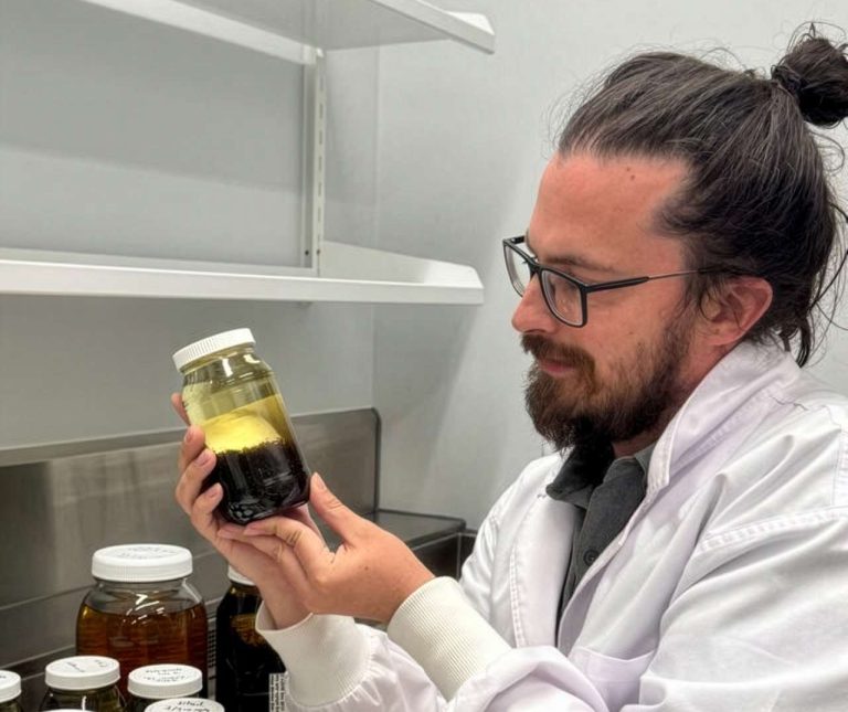 Person with beard and glasses holding jar of flies.