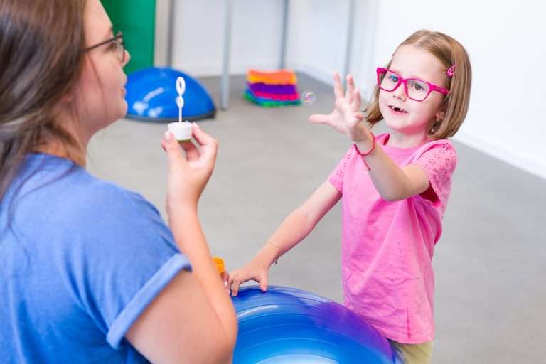 Child with physical disability in bilateral coordination physiotherapy. Child living with cerebral palsy exercising with her therapist.