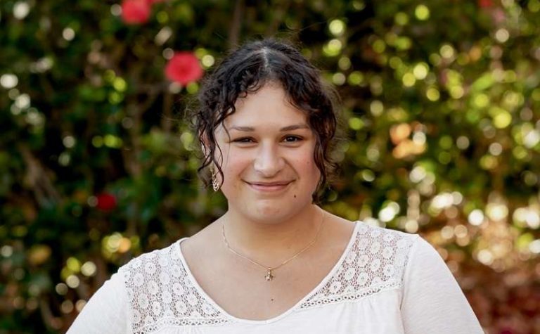 Woman with dark curly hair wearing white shirt