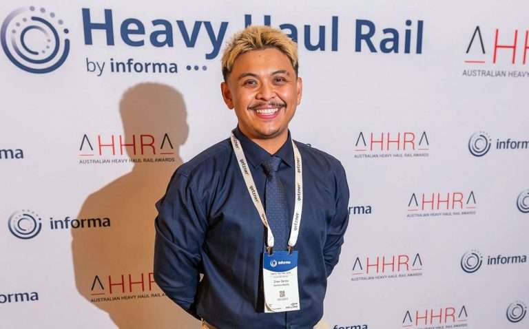 Man with moustache and bleached blonde hair in a blue collared shirt