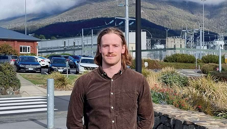 Man with long hair and brown shirt standing in front of power lines