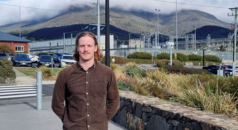 Man with long hair and brown shirt standing in front of power lines