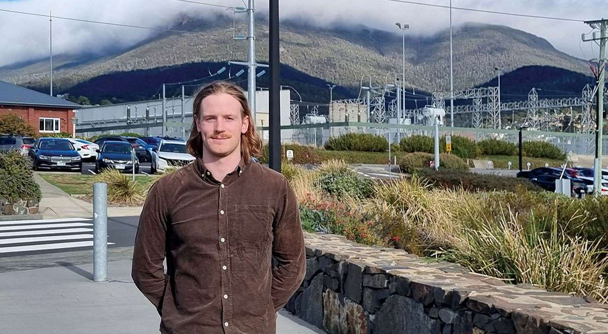 Man with long hair and brown shirt standing in front of power lines