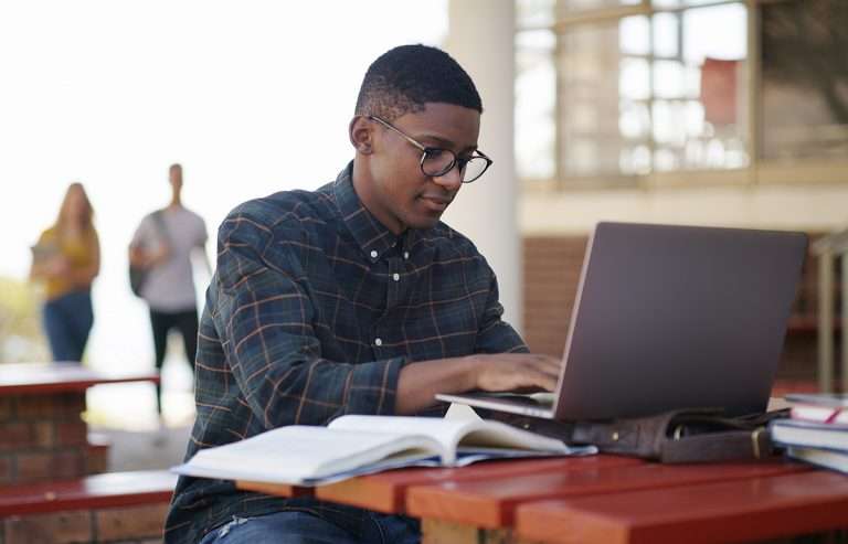 Student, typing and man in campus with laptop, test and research for project deadline. Preparation, multitask and scholar with study material, brainstorm and problem solve for academic goals.