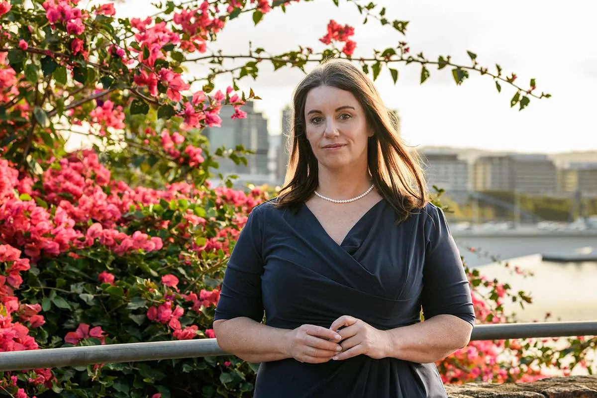 Woman in dress with long brown hair in front of red bougainvillaea
