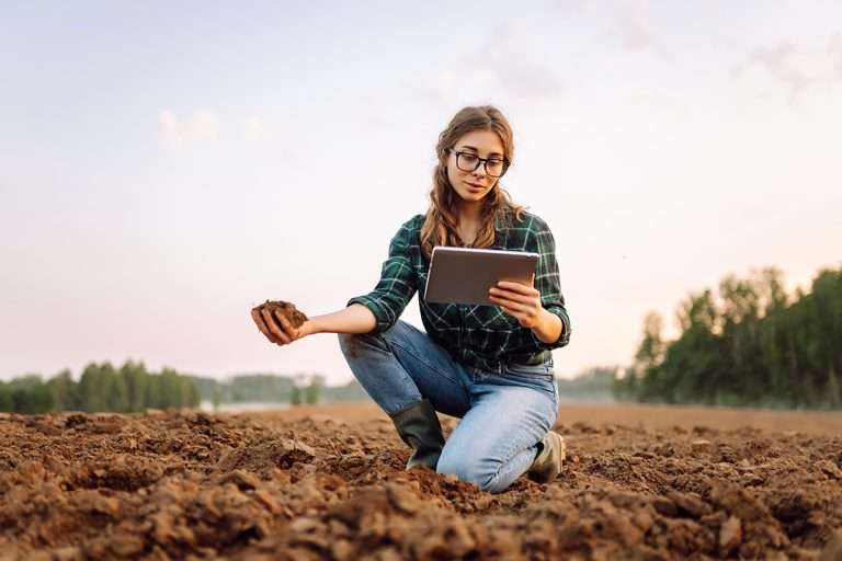 Woman checking soil, holding iPad